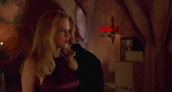 Movie still from “Batman Forever” (1995), directed by Joel Schumacher – A woman with blonde hair sitting in a room; Medium shot, Low angle