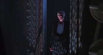 Movie still from “Batman Forever” (1995), directed by Joel Schumacher – An old man in a suit standing in front of a wall; Wide shot, Low angle