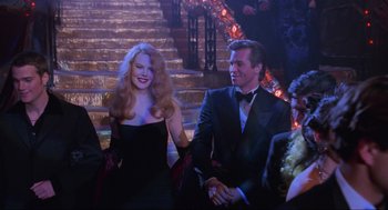 Movie still from “Batman Forever” (1995), directed by Joel Schumacher – A man and a woman in formal wear standing next to each other in front of a staircase; Medium shot, Over the shoulder angle