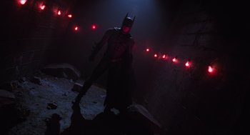 Movie still from “Batman Forever” (1995), directed by Joel Schumacher – A man dressed as batman standing in a dark room; Wide shot, Low angle