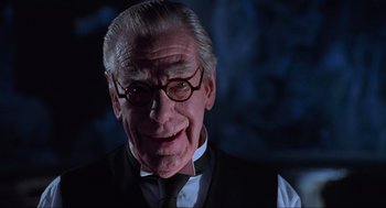 Movie still from “Batman Forever” (1995), directed by Joel Schumacher – An older man wearing glasses and a tie; Close Up shot, Low angle