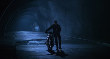 Movie still from “Batman Forever” (1995), directed by Joel Schumacher – A man standing next to a motorcycle in a tunnel; Wide shot, Low angle