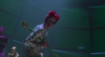 Movie still from “Batman Forever” (1995), directed by Joel Schumacher – A man with pink hair holding a pole; Medium shot, Low angle