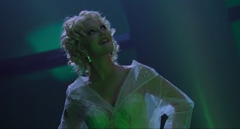 Movie still from “Batman Forever” (1995), directed by Joel Schumacher – A woman with blonde curly hair wearing a white dress; Medium shot, Low angle