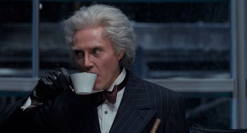 Movie still from “Batman Returns” (1992), directed by Tim Burton – A man in a suit and tie drinking a cup of coffee; Medium shot, Low angle