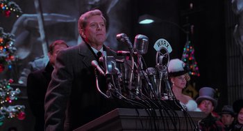 Movie still from “Batman Returns” (1992), directed by Tim Burton – A man standing at a podium with many microphones; Medium shot, Low angle