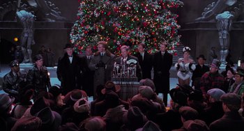 Movie still from “Batman Returns” (1992), directed by Tim Burton – A group of people standing in front of a christmas tree; Wide shot, Low angle
