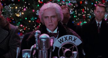 Movie still from “Batman Returns” (1992), directed by Tim Burton – A man in a suit and tie sitting at a microphone; Close Up shot, Low angle