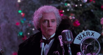 Movie still from “Batman Returns” (1992), directed by Tim Burton – A man in a suit and tie next to a microphone; Close Up shot, Over the shoulder angle