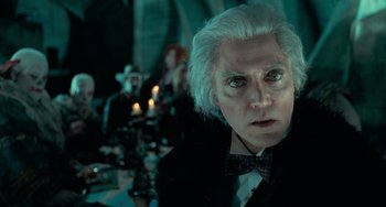 Movie still from “Batman Returns” (1992), directed by Tim Burton – An old man with white hair and a bow tie; Close Up shot, Over the shoulder angle