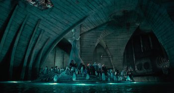 Movie still from “Batman Returns” (1992), directed by Tim Burton – A group of people sitting on steps near a body of water; Extreme Wide shot, Low angle