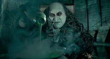 Movie still from “Batman Returns” (1992), directed by Tim Burton – A man dressed as the evil wizard grindelwald pouring green liquid into a bottle; Close Up shot, Low angle