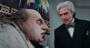 Movie still from “Batman Returns” (1992), directed by Tim Burton – A man standing next to another man in a suit and tie; Close Up shot, Over the shoulder angle
