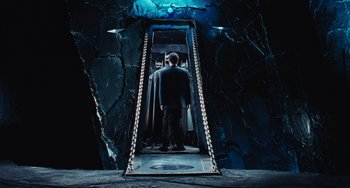 Movie still from “Batman Returns” (1992), directed by Tim Burton – A man in a suit standing in front of an open door; Wide shot, High angle