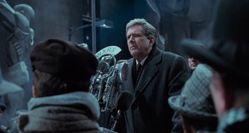Movie still from “Batman Returns” (1992), directed by Tim Burton – A man in a suit and tie speaking into a microphone; Close Up shot, Low angle