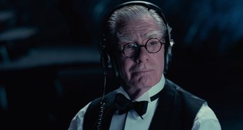 Movie still from “Batman Returns” (1992), directed by Tim Burton – An older man wearing headphones and a bow tie; Close Up shot, Over the shoulder angle