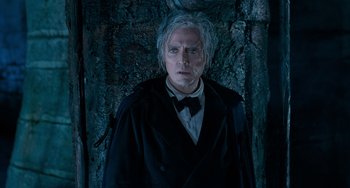 Movie still from “Batman Returns” (1992), directed by Tim Burton – A man in a black coat and a bow tie standing in front of a tree; Medium shot, High angle