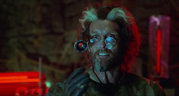 Movie still from “Batman & Robin” (1997), directed by Joel Schumacher – A man with a beard and glasses is holding a magnifying glass in his hand; Close Up shot, Over the shoulder angle