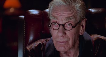 Movie still from “Batman & Robin” (1997), directed by Joel Schumacher – An older man with glasses sitting in a chair; Close Up shot, Low angle