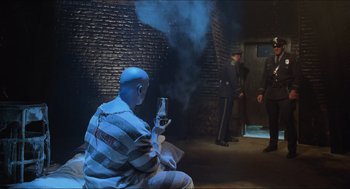 Movie still from “Batman & Robin” (1997), directed by Joel Schumacher – A man in a prison uniform holding a glass of wine; Wide shot, High angle