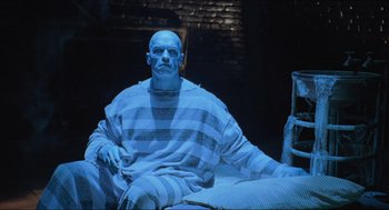 Movie still from “Batman & Robin” (1997), directed by Joel Schumacher – A bald man sitting on top of a bed in front of a brick wall; Medium shot, High angle