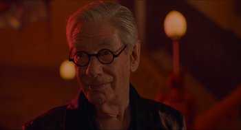Movie still from “Batman & Robin” (1997), directed by Joel Schumacher – An older man wearing glasses and smiling for the camera; Close Up shot, Over the shoulder angle
