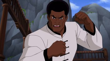 Movie still from “Batman: Soul of the Dragon” (2021), directed by Sam Liu – A man in white shirt and black hat with fist in the air; Medium shot, Low angle