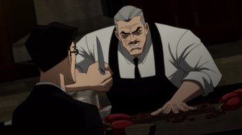 Movie still from “Batman: The Long Halloween” (2021), directed by Chris Palmer – An older man holding a knife in front of a woman; Medium shot, Over the shoulder angle