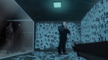 Movie still from “Batman: The Long Halloween” (2021), directed by Chris Palmer – A man standing in front of a wall covered in numbers; Wide shot, High angle