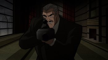 Movie still from “Batman: The Long Halloween” (2021), directed by Chris Palmer – An older man holding a camera in a dark room; Medium shot, Over the shoulder angle