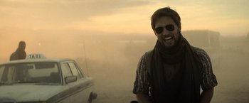 Movie still from “Batman v Superman: Dawn of Justice” (2016), directed by Zack Snyder – A man with sunglasses and a scarf smiles for the camera; Medium shot, Over the shoulder angle