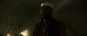 Movie still from “Batman v Superman: Dawn of Justice” (2016), directed by Zack Snyder – A man with a white hat is standing in a dark room; Close Up shot, Low angle