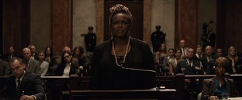 Movie still from “Batman v Superman: Dawn of Justice” (2016), directed by Zack Snyder – A woman standing in front of a microphone in a courtroom; Medium shot, Low angle
