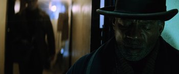 Movie still from “Batman v Superman: Dawn of Justice” (2016), directed by Zack Snyder – A man wearing a hat standing next to a window; Close Up shot, Low angle