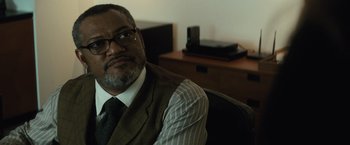 Movie still from “Batman v Superman: Dawn of Justice” (2016), directed by Zack Snyder – A man sitting in a chair wearing a suit and tie; Close Up shot, Over the shoulder angle