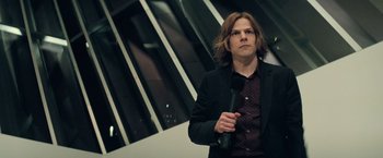 Movie still from “Batman v Superman: Dawn of Justice” (2016), directed by Zack Snyder – A man with long brown hair holding a microphone in his hand; Medium shot, Over the shoulder angle