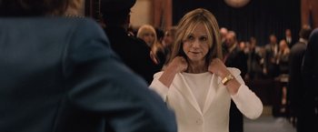 Movie still from “Batman v Superman: Dawn of Justice” (2016), directed by Zack Snyder – A woman adjusts the collar of a white jacket; Medium shot, Over the shoulder angle