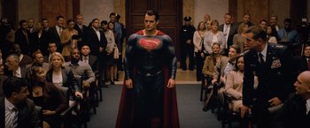 Movie still from “Batman v Superman: Dawn of Justice” (2016), directed by Zack Snyder – A man in a superman suit stands in front of a group of people; Wide shot, Over the shoulder angle