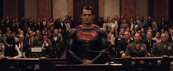 Movie still from “Batman v Superman: Dawn of Justice” (2016), directed by Zack Snyder – A man wearing a superman suit stands in front of a crowd of onlookers in a courtroom; Medium shot, Low angle