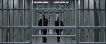 Movie still from “Batman v Superman: Dawn of Justice” (2016), directed by Zack Snyder – Two men in suits are walking through a jail cell; Wide shot, Low angle