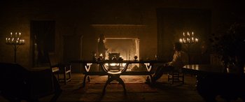 Movie still from “The Last Duel” (2021), directed by Ridley Scott – Two people sitting at a table in front of a fireplace; Extreme Wide shot, Over the shoulder angle