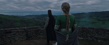 Movie still from “The Last Duel” (2021), directed by Ridley Scott – A woman in a green dress standing next to a man in a black cloak; Medium shot, Over the shoulder angle