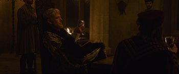 Movie still from “The Last Duel” (2021), directed by Ridley Scott – A man holding a wine glass sitting on a couch; Medium shot, Over the shoulder angle
