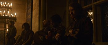 Movie still from “The Last Duel” (2021), directed by Ridley Scott – A group of men playing musical instruments in a dark room; Medium shot, Low angle