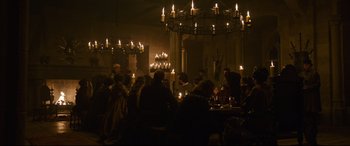 Movie still from “The Last Duel” (2021), directed by Ridley Scott – A group of people sitting at a table in front of candles; Wide shot, High angle