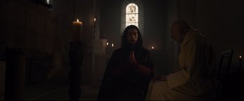 Movie still from “The Last Duel” (2021), directed by Ridley Scott – A person in a dark room with candles; Medium shot, Low angle