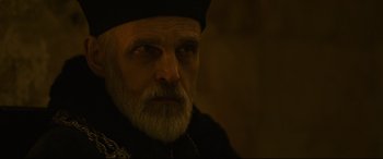 Movie still from “The Last Duel” (2021), directed by Ridley Scott – An old man with a beard wearing a black hat; Close Up shot, Over the shoulder angle