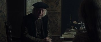 Movie still from “The Last Duel” (2021), directed by Ridley Scott – An older man sitting in front of a table; Medium shot, Over the shoulder angle