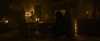 Movie still from “The Last Duel” (2021), directed by Ridley Scott – A group of people sitting around a table with candles; Wide shot, Low angle