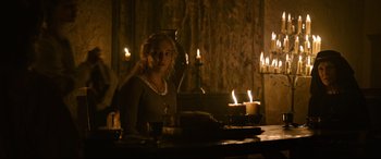 Movie still from “The Last Duel” (2021), directed by Ridley Scott – A woman standing in front of candles in a room; Medium shot, Over the shoulder angle